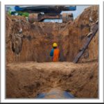 Construction worker working in trench while watching digger.
